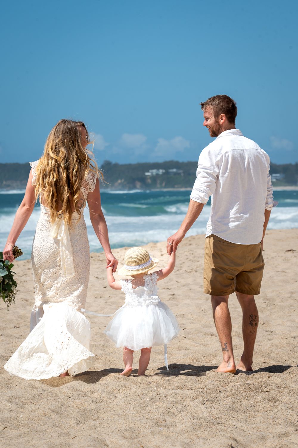 Bride and Groom holding their flower girls hand walking on the beach