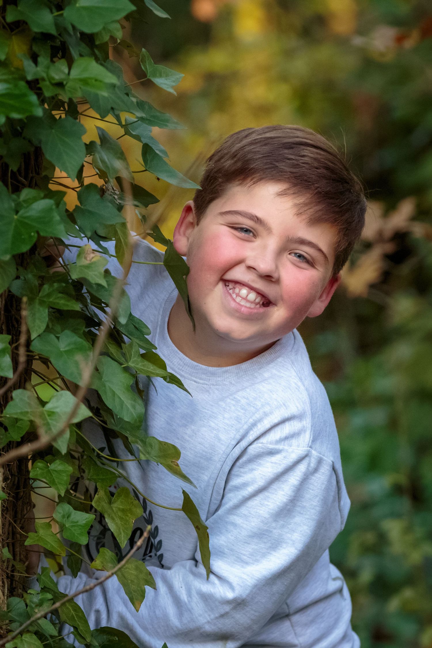 portrait of a young boy smiling and leaning against a large tree