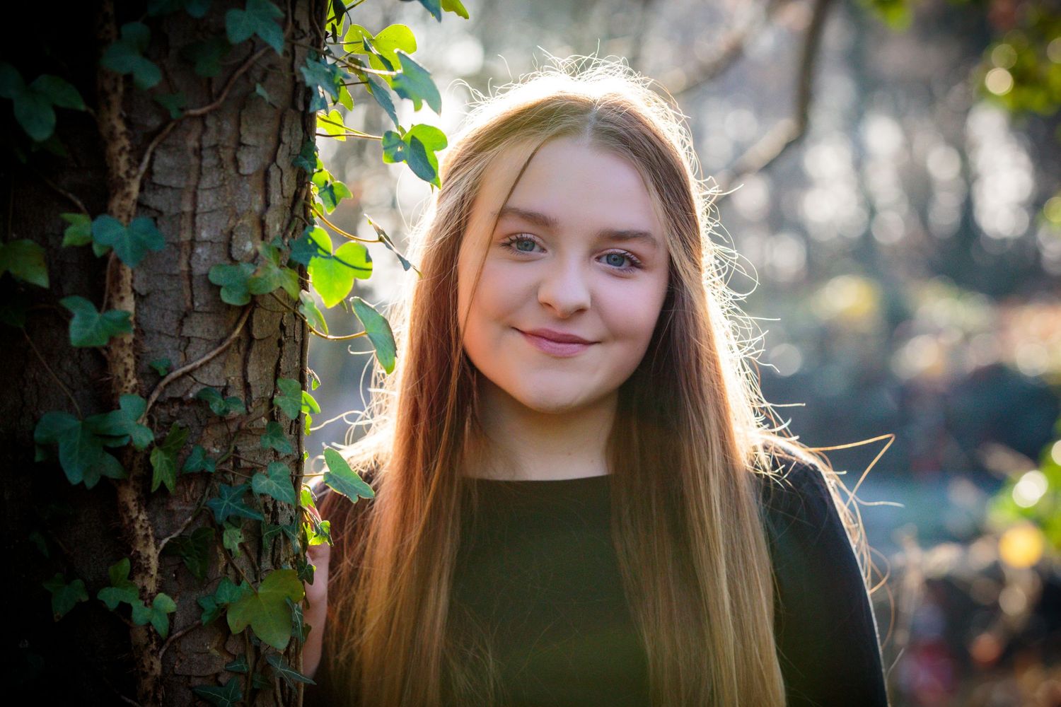 portrait of a teenage girl standing next to a large tree covered in ivy