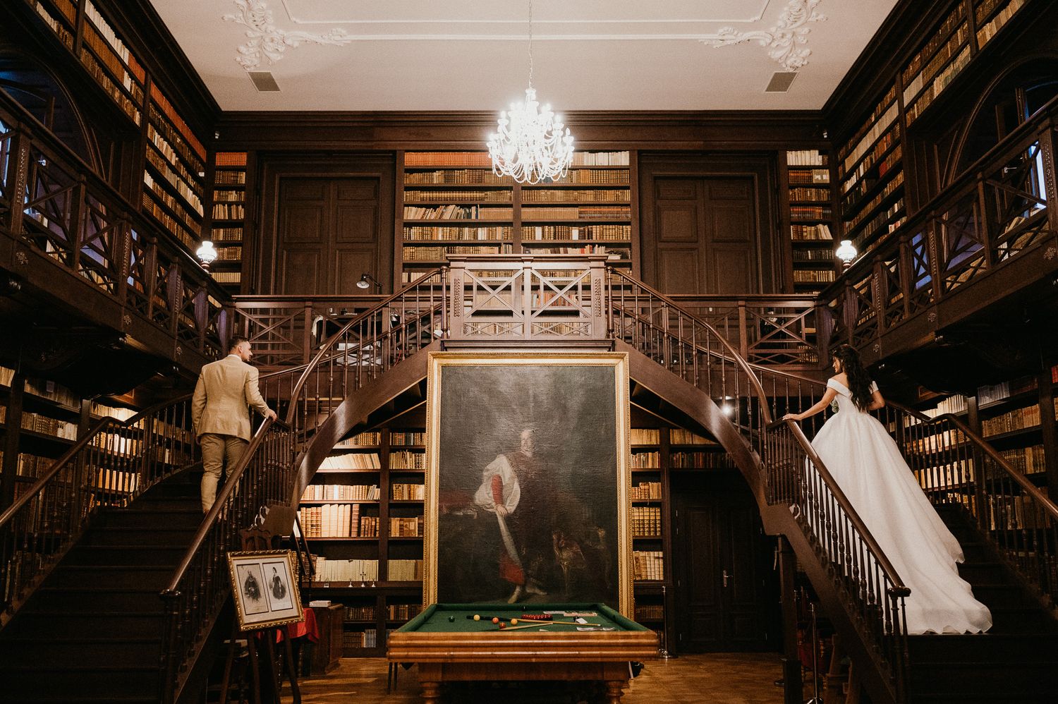 Ornate library interior with wooden staircase, chandelier and wedding dress.