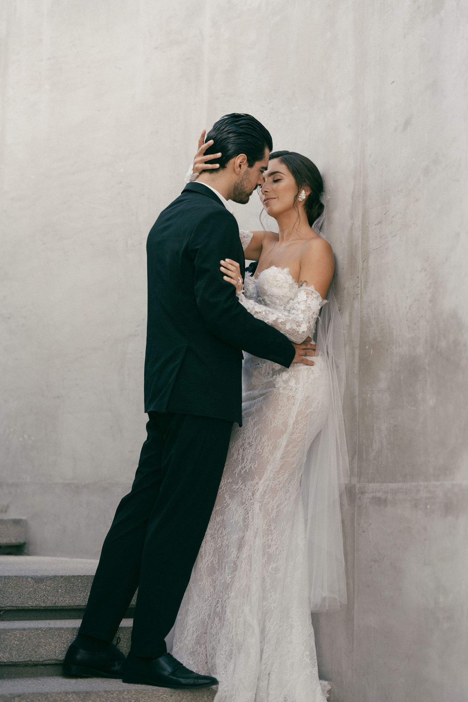 An intimate wedding portrait of a couple in an elegant embrace against a neutral wall.