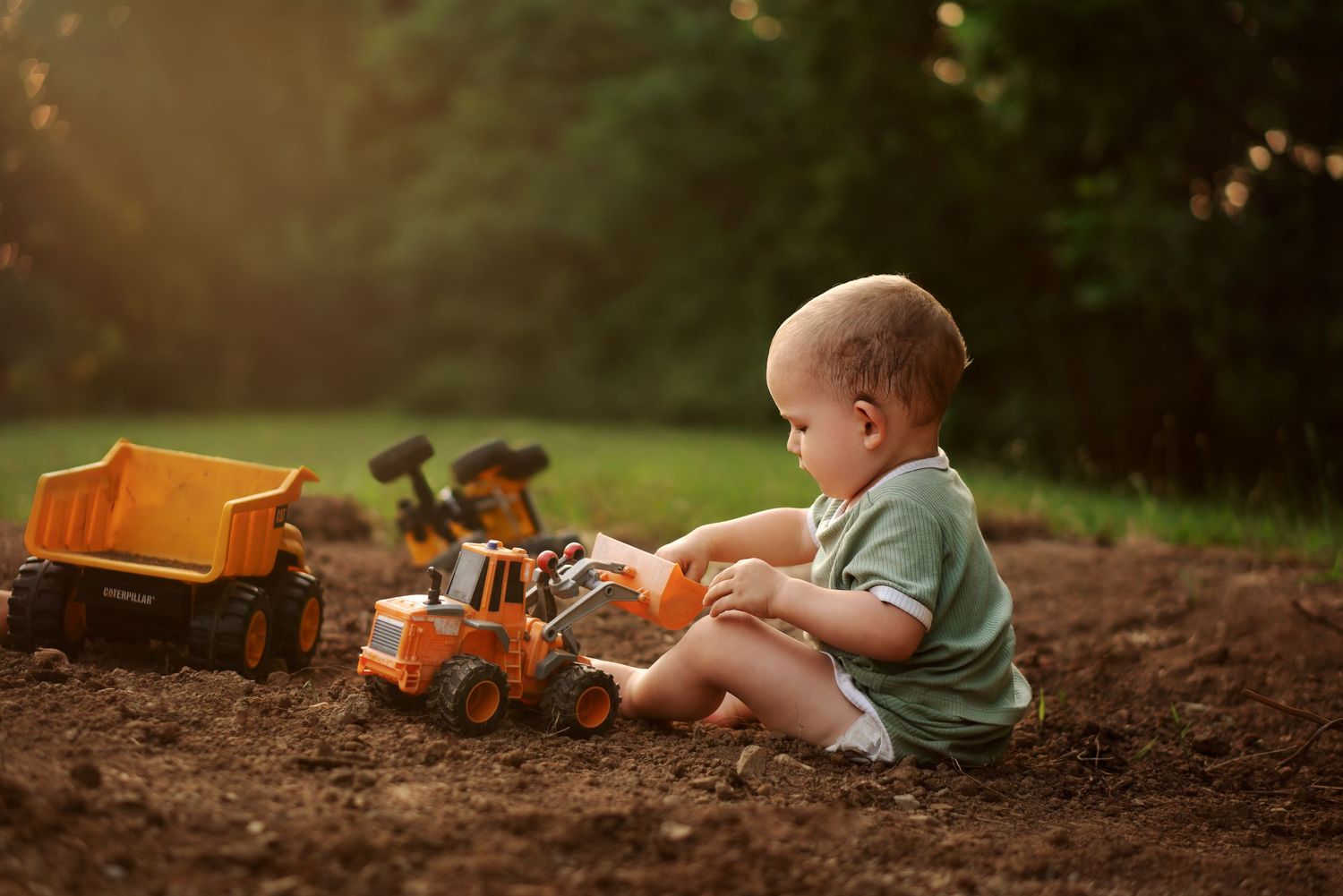toddler boy plays in dirt with construction equipment toys