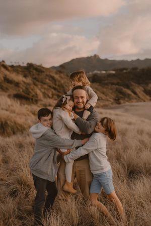 kids climbing on dad in amongst the dunes in raglan beach for family photoshoot