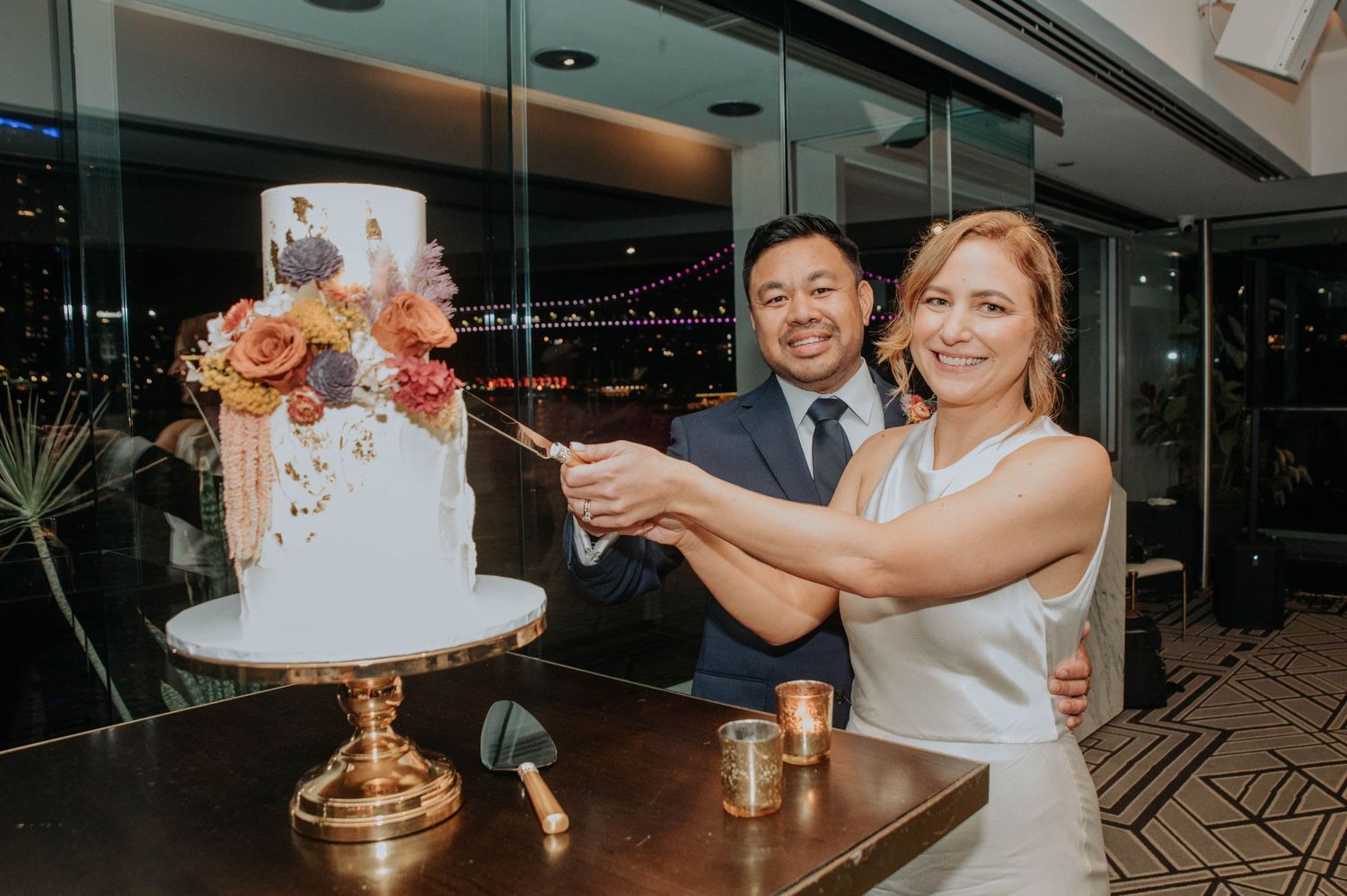 Wedding couple cuts elegant white and coral floral wedding cake at reception.