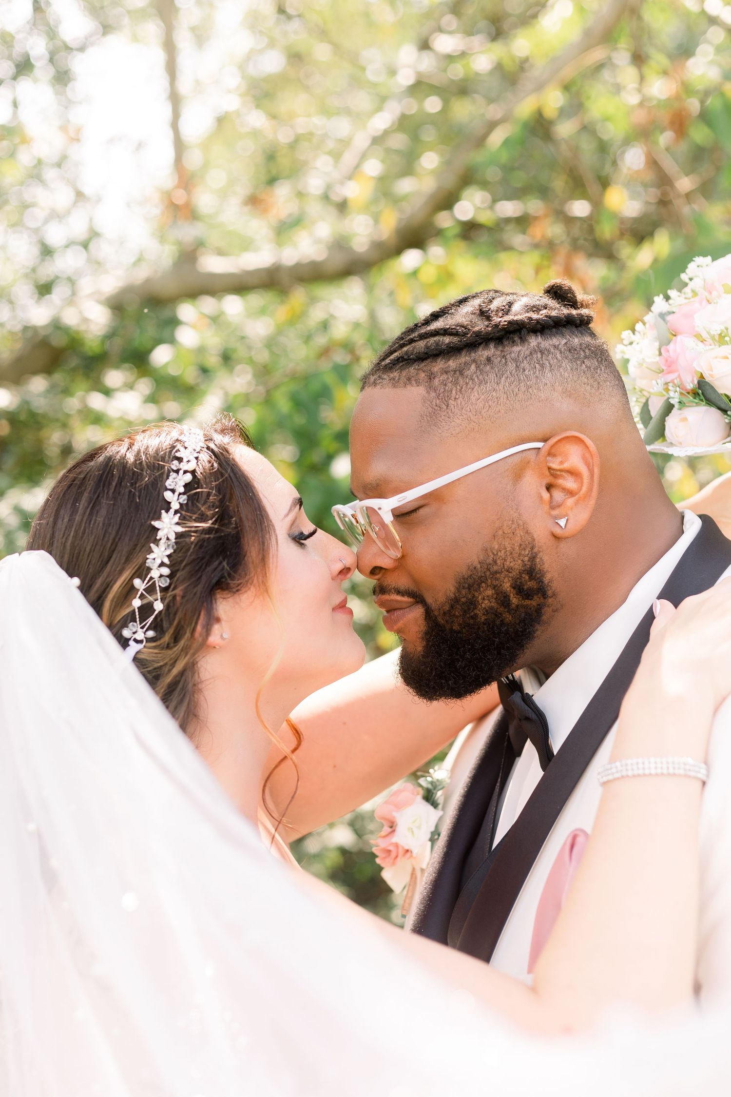 Romantic wedding portrait in a sun-dappled garden setting with delicate hair accessories.