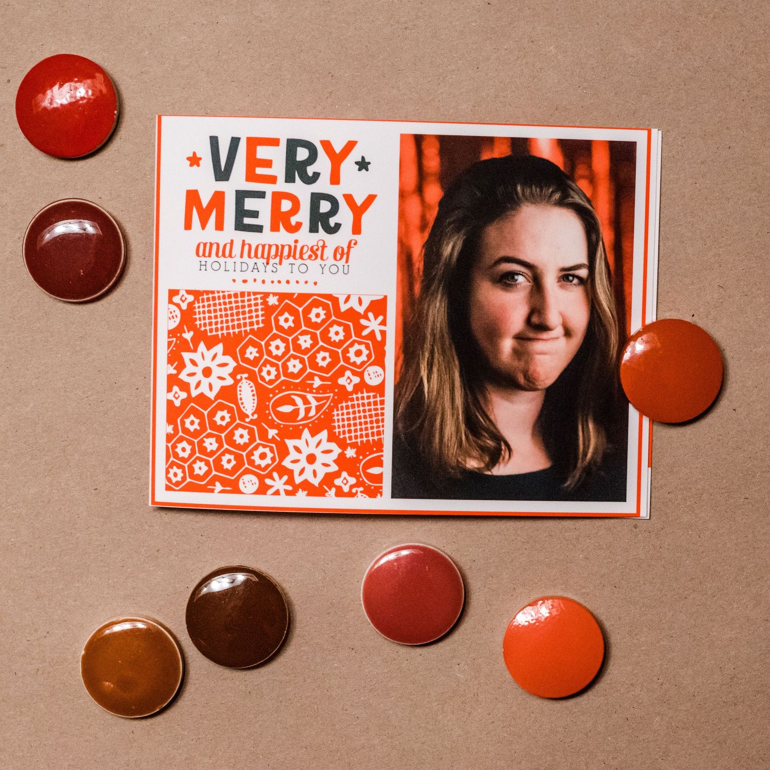 Holiday card with red and blue lettering surrounded by chocolate candies on brown background.