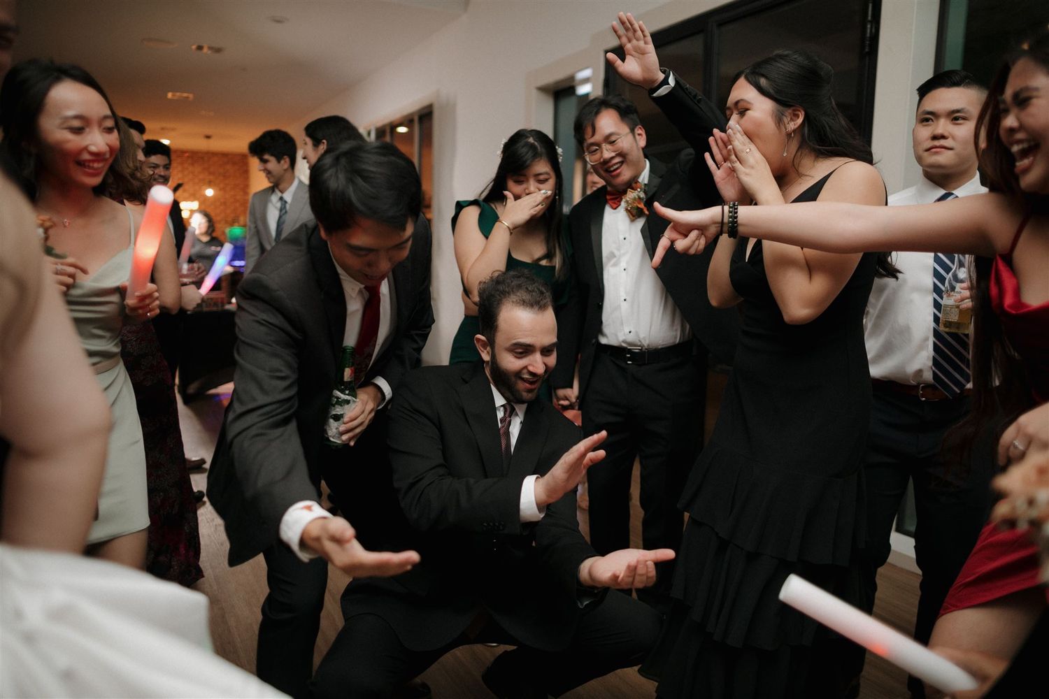 Wedding guests dancing enthusiastically in formal attire at an indoor celebration.