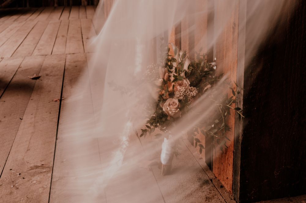 A delicate veil drapes over dried floral arrangements on a rustic wooden floor in moody lighting.