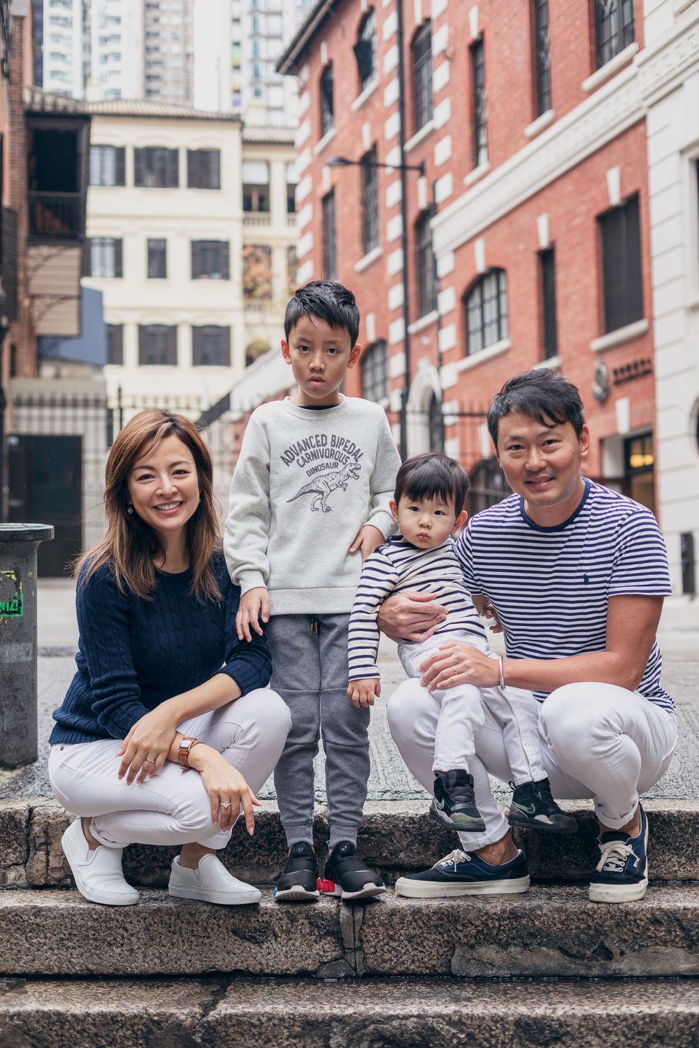 A family portrait on urban stone steps with brick buildings in the background.