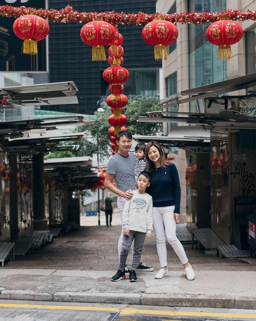 Family poses beneath traditional red Chinese lanterns in an urban shopping district.