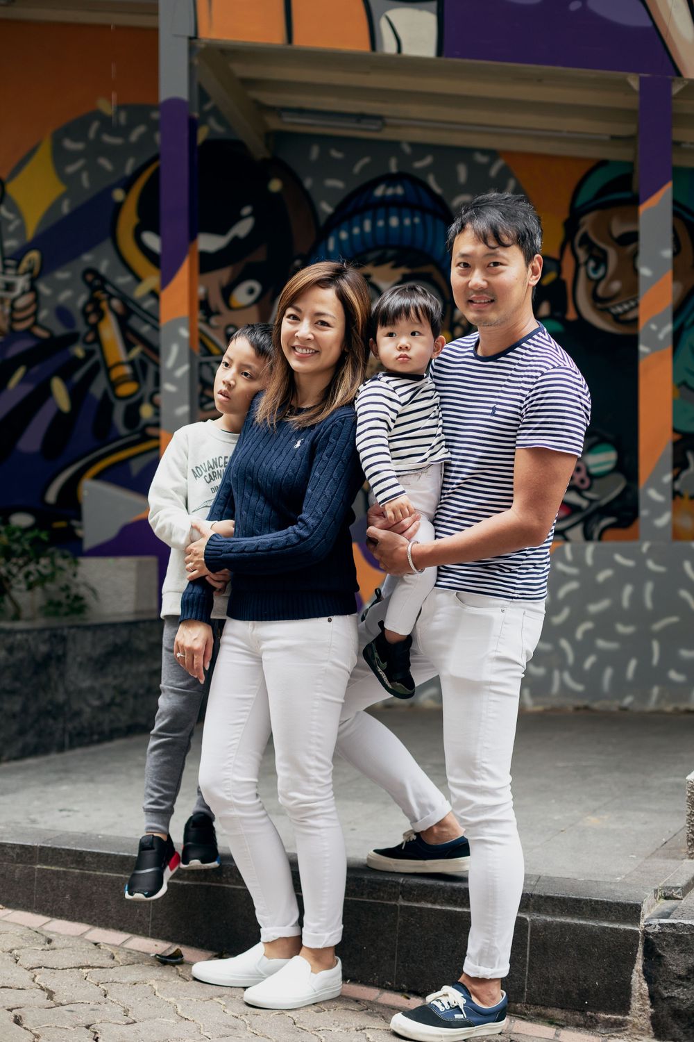 Coordinated family wearing matching white and navy outfits against colorful wall art.