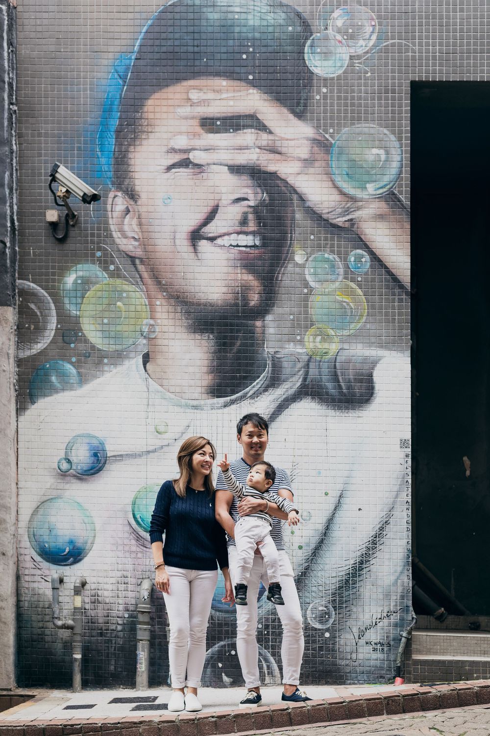 Family poses against street art mural featuring soap bubbles on grey wall.