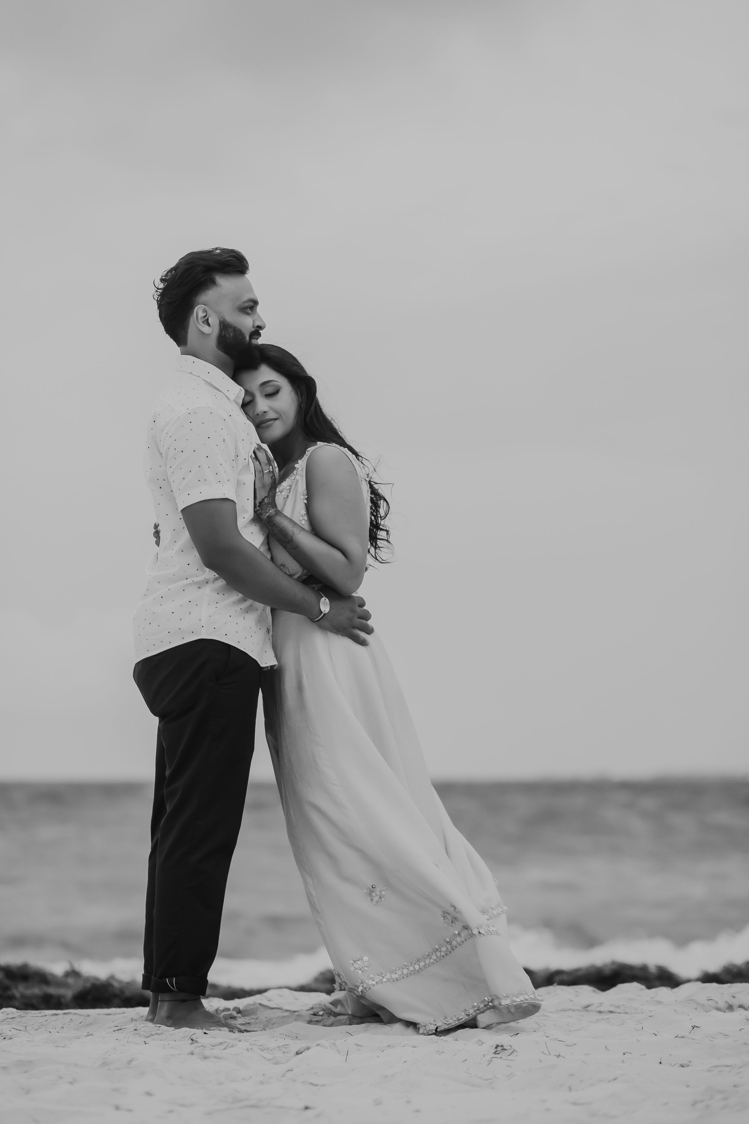 A couple embraces on a beach in black and white photography.