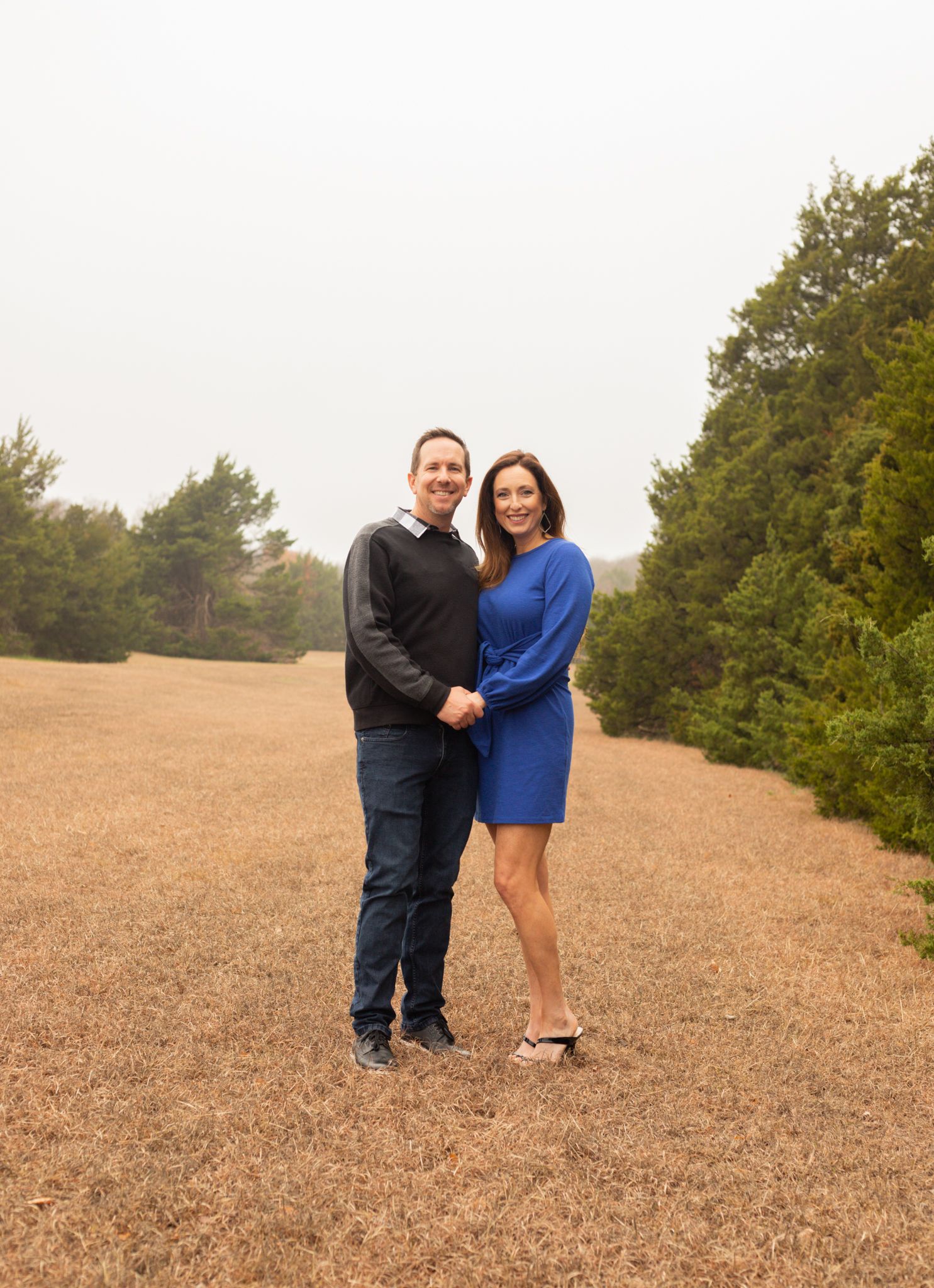 Couple in blue and black outfits smiling together in misty outdoor field setting.