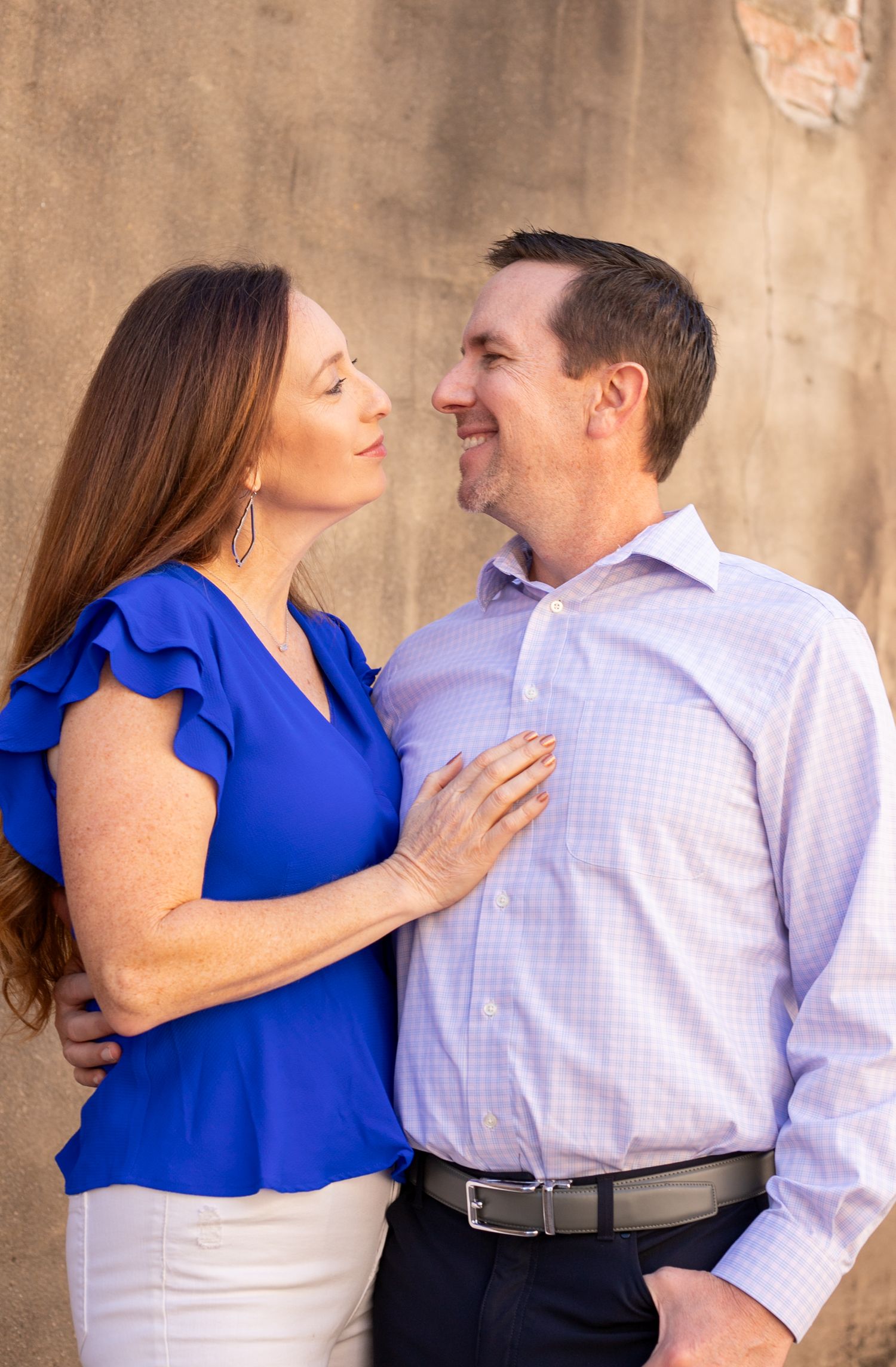 Couple in blue and white outfits sharing a romantic moment against a textured tan wall.