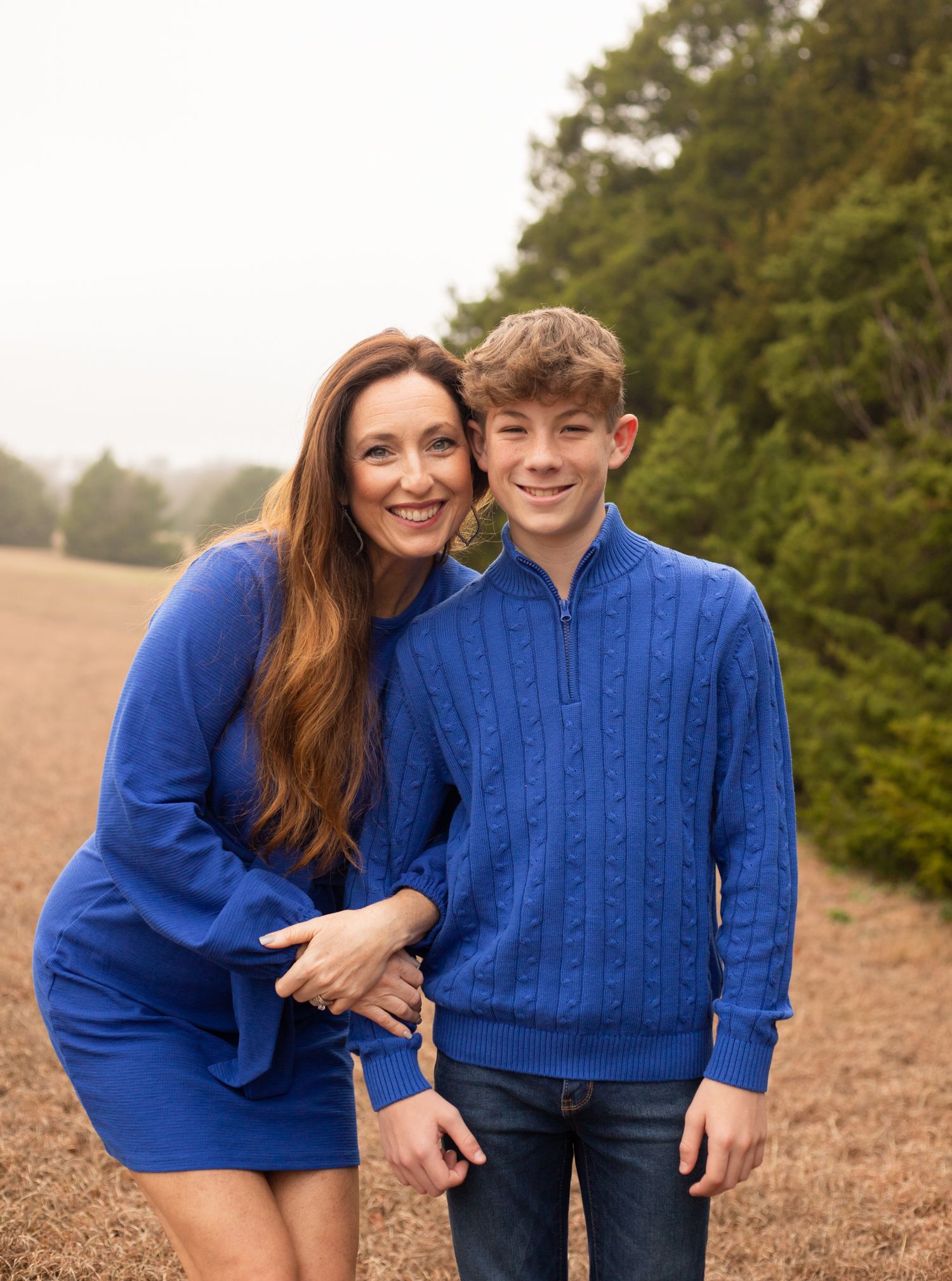 Mother and son in matching blue outfits posing together for a family portrait in an open field.