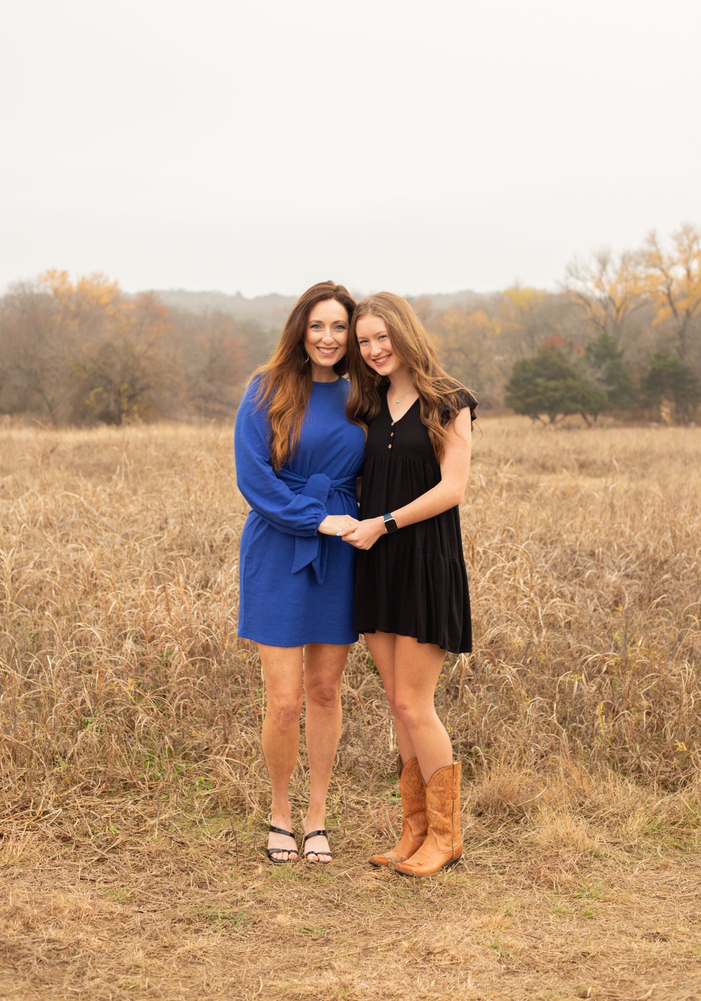 Mother and teenage daughter in blue and black dresses posing in autumn field.