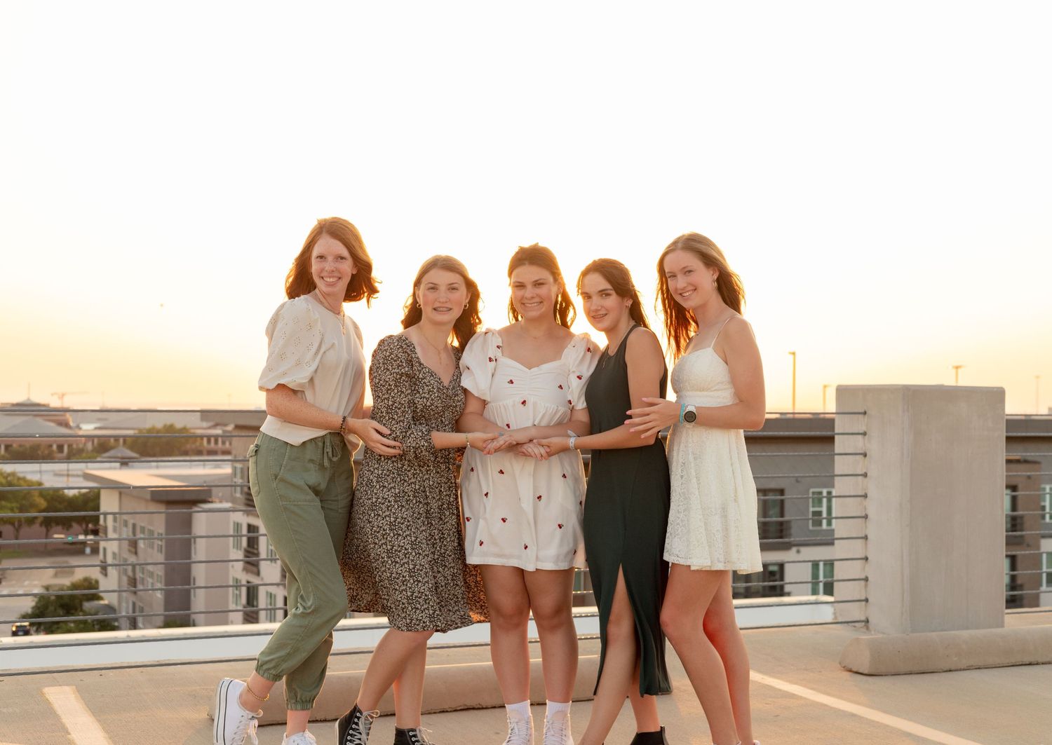 Group of five teenage girls posing together on a rooftop at sunset.