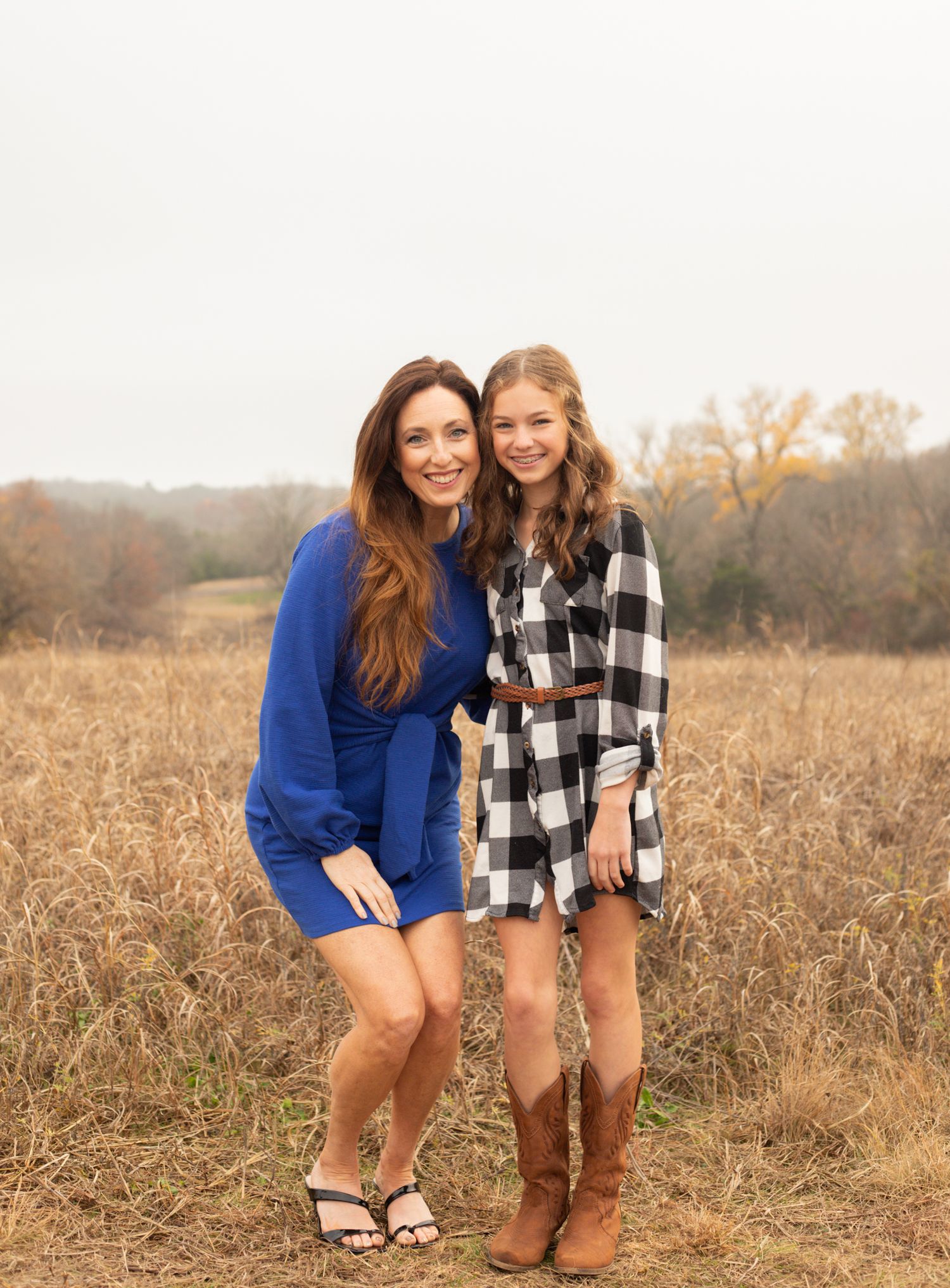 Mother and daughter smiling together in blue dress and plaid outfit in fall field.