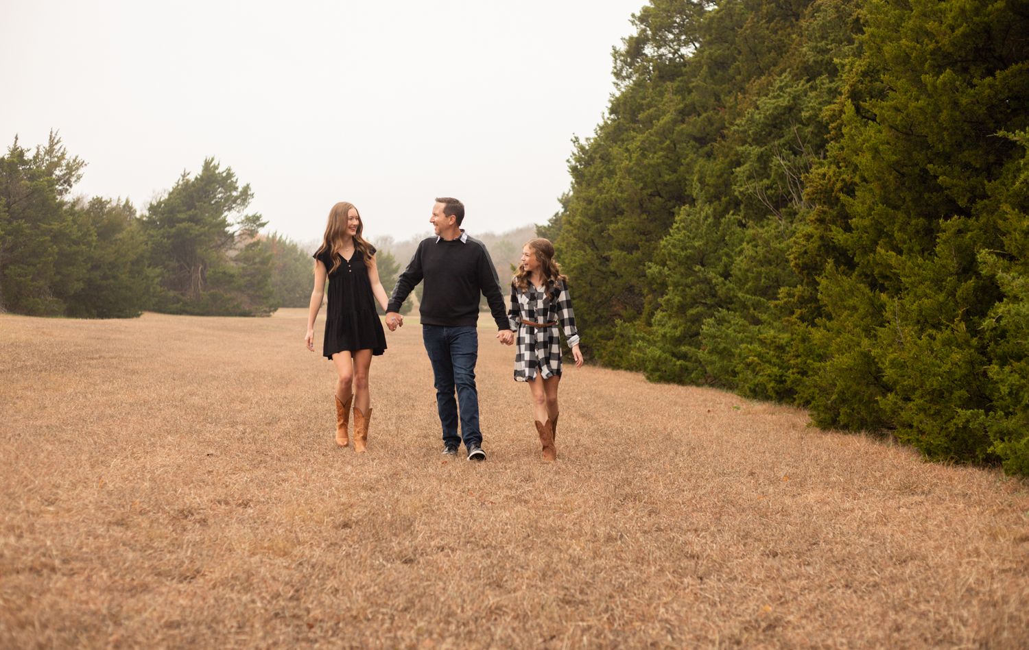 Father walking hand in hand with two daughters through a golden field during a family photo session.