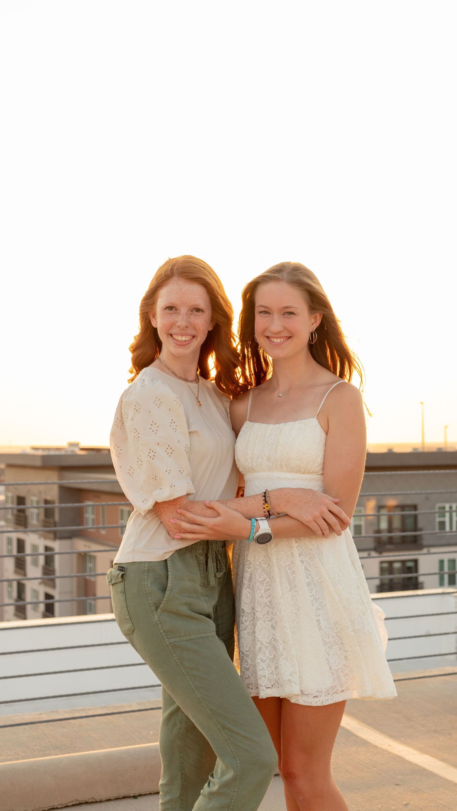 Two teenage girls posing together on a rooftop during a warm sunset.