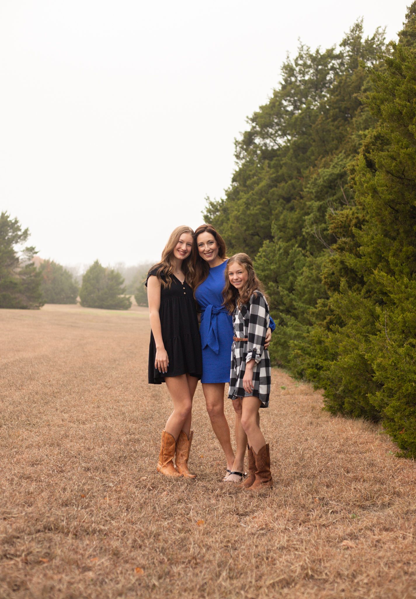 Three girls posing together in a field wearing coordinating outfits including cowboy boots and dresses.