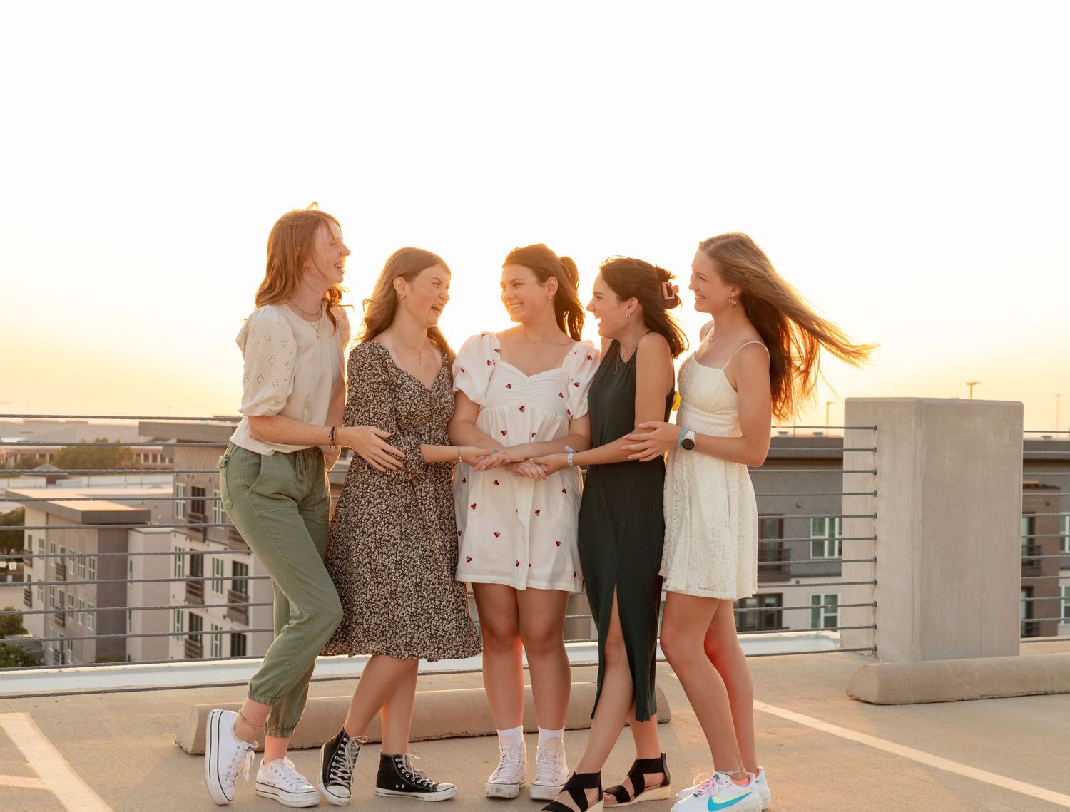 Five teenage girls laughing and posing on a rooftop during golden hour.