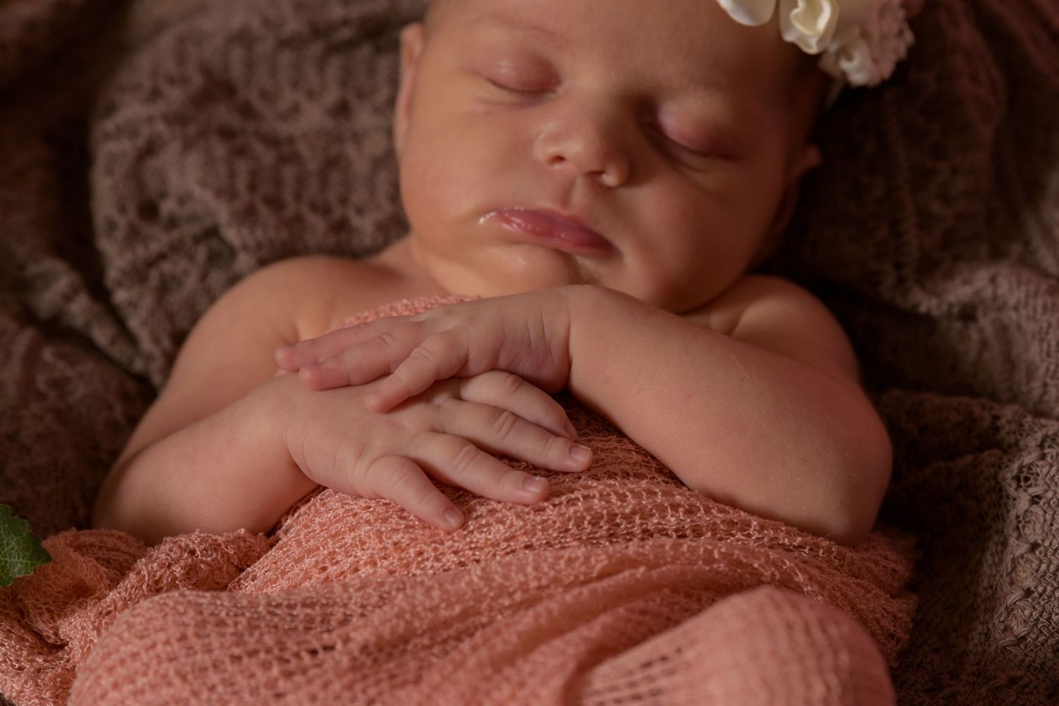 A sleeping newborn baby girl wrapped in pink with a floral headband closeup portrait.