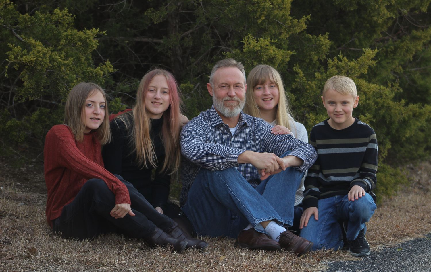 A man sits with four children for an outdoor family portrait surrounded by greenery.