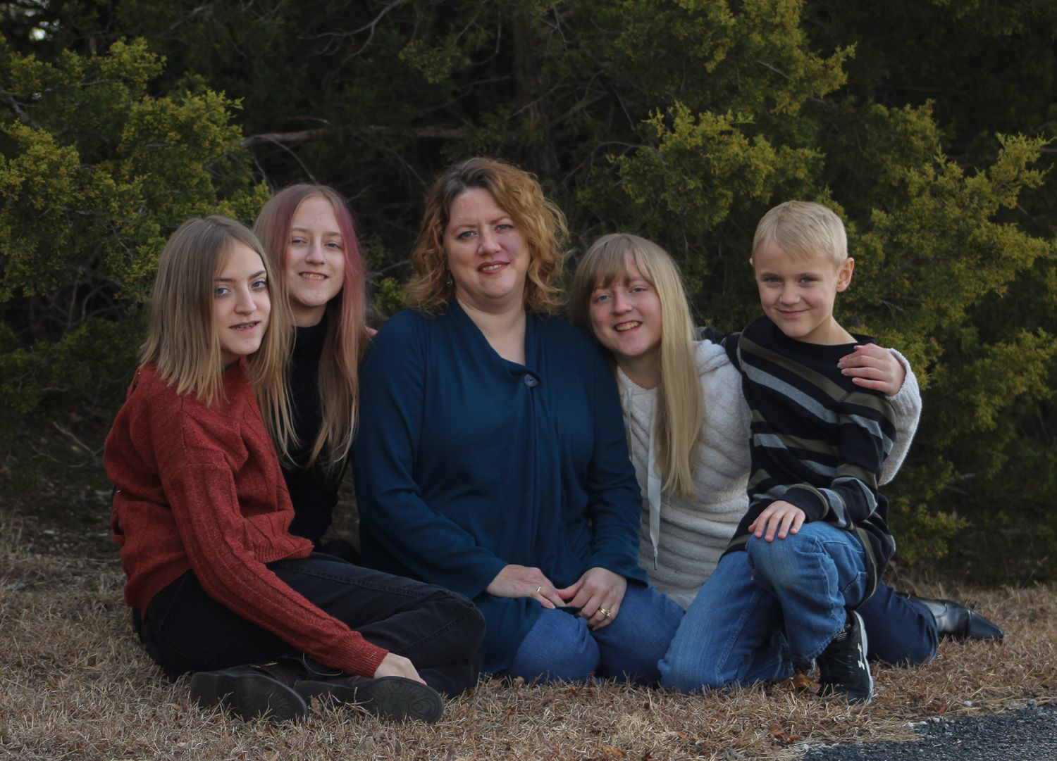 A woman poses with four children outdoors in a family portrait among green trees.