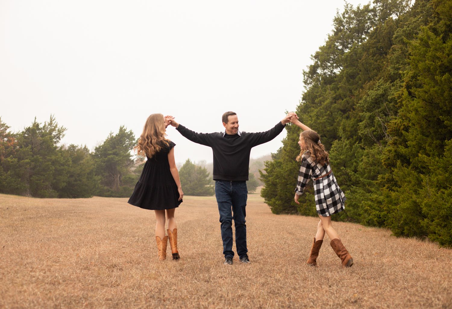 Father joyfully swinging his two daughters by their hands in an open golden field outdoors.