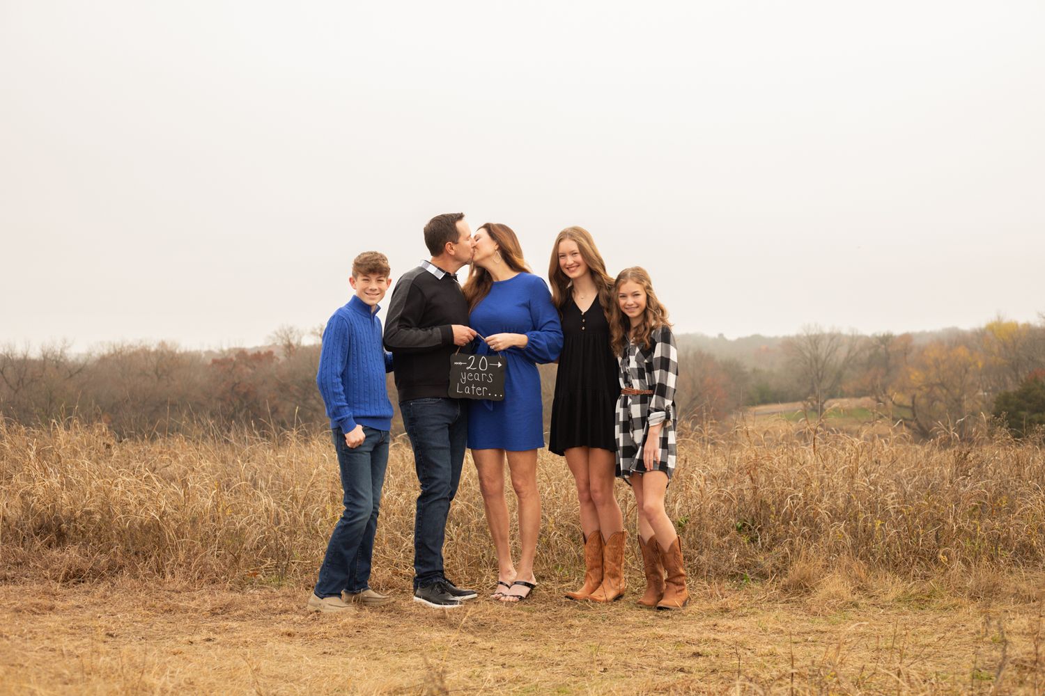 Family of five posing and sharing a kiss in an open autumn field.