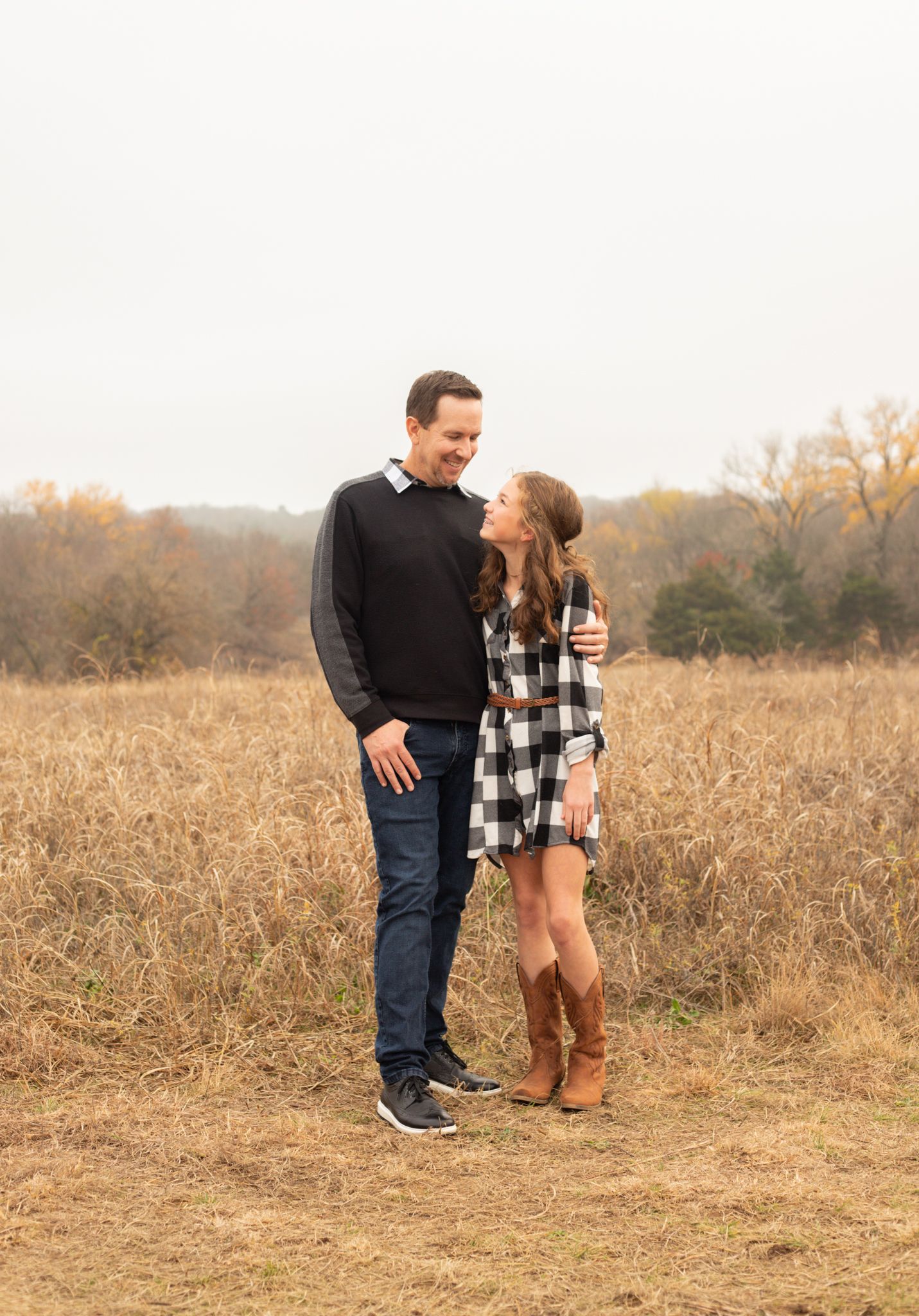 Father and daughter in plaid dress sharing a smile in golden autumn field.