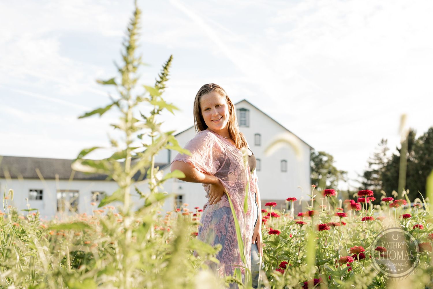 A summer portrait among tall wildflowers and red poppies with a white farmhouse behind.