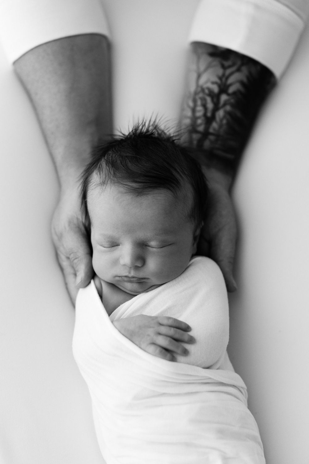 Black and white newborn natural light image. Swaddled newborn in father's arms. Natural light image by Jen Roberts in Phoenix, AZ