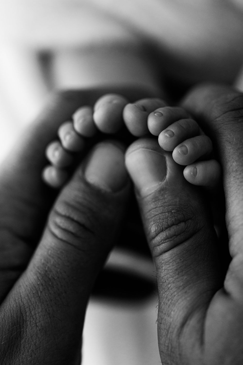 Detailed, black and white image of newborn toes being held in father's hands. Macro photography, Jen Roberts photographer in Mesa, AZ