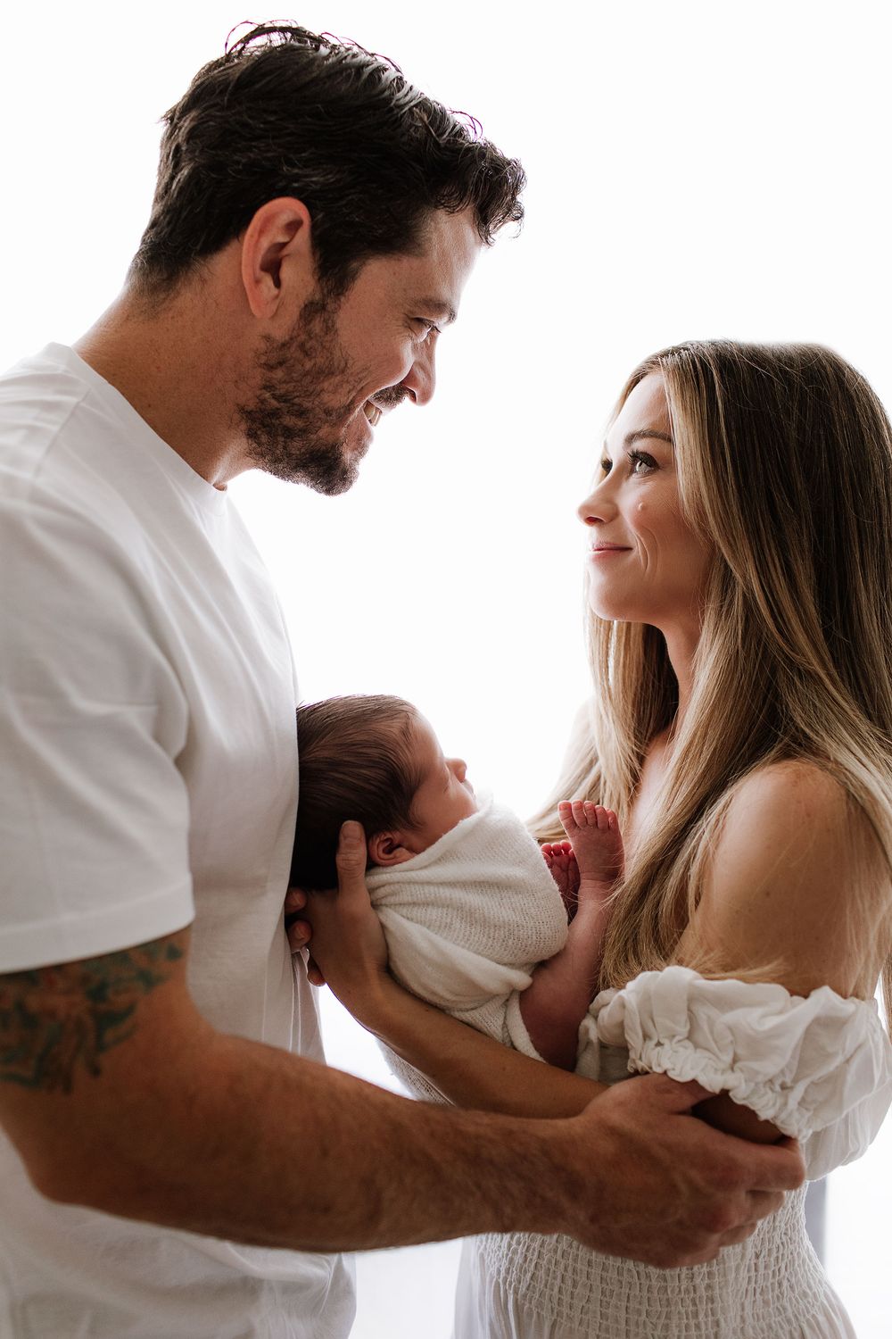 Backlit photo of mother and father looking at each other with mother holding newborn. Studio photo by Jen Roberts photographer in Gilbert