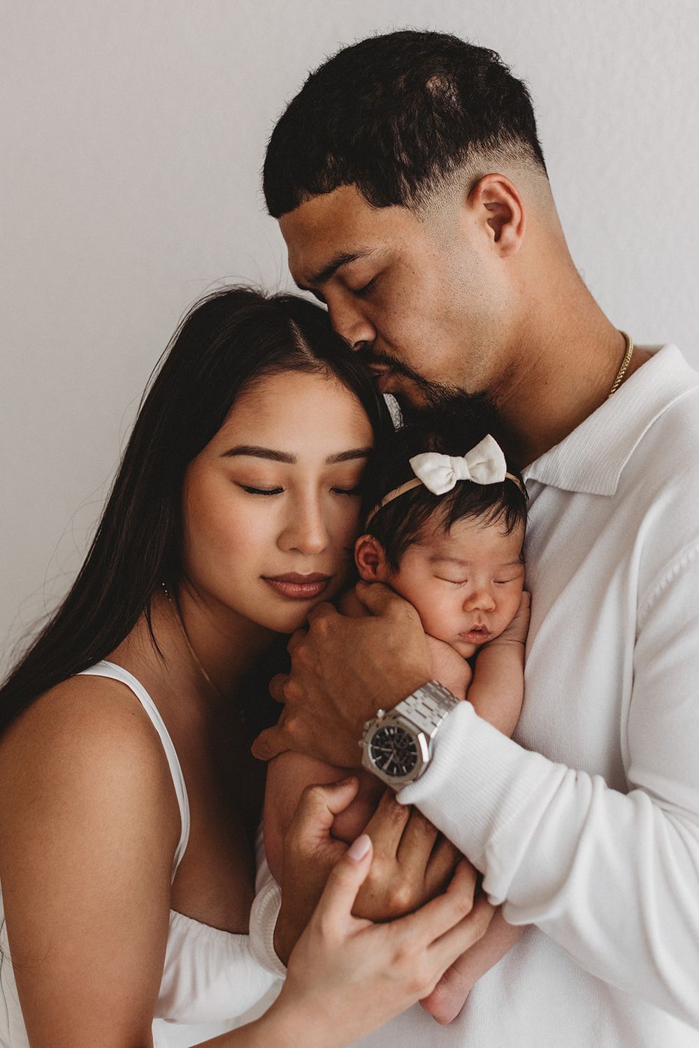 Newborn photo highlighting mother and father cuddling newborn. Father kisses mother's forehead. Natural image by Jen Roberts in Arizona