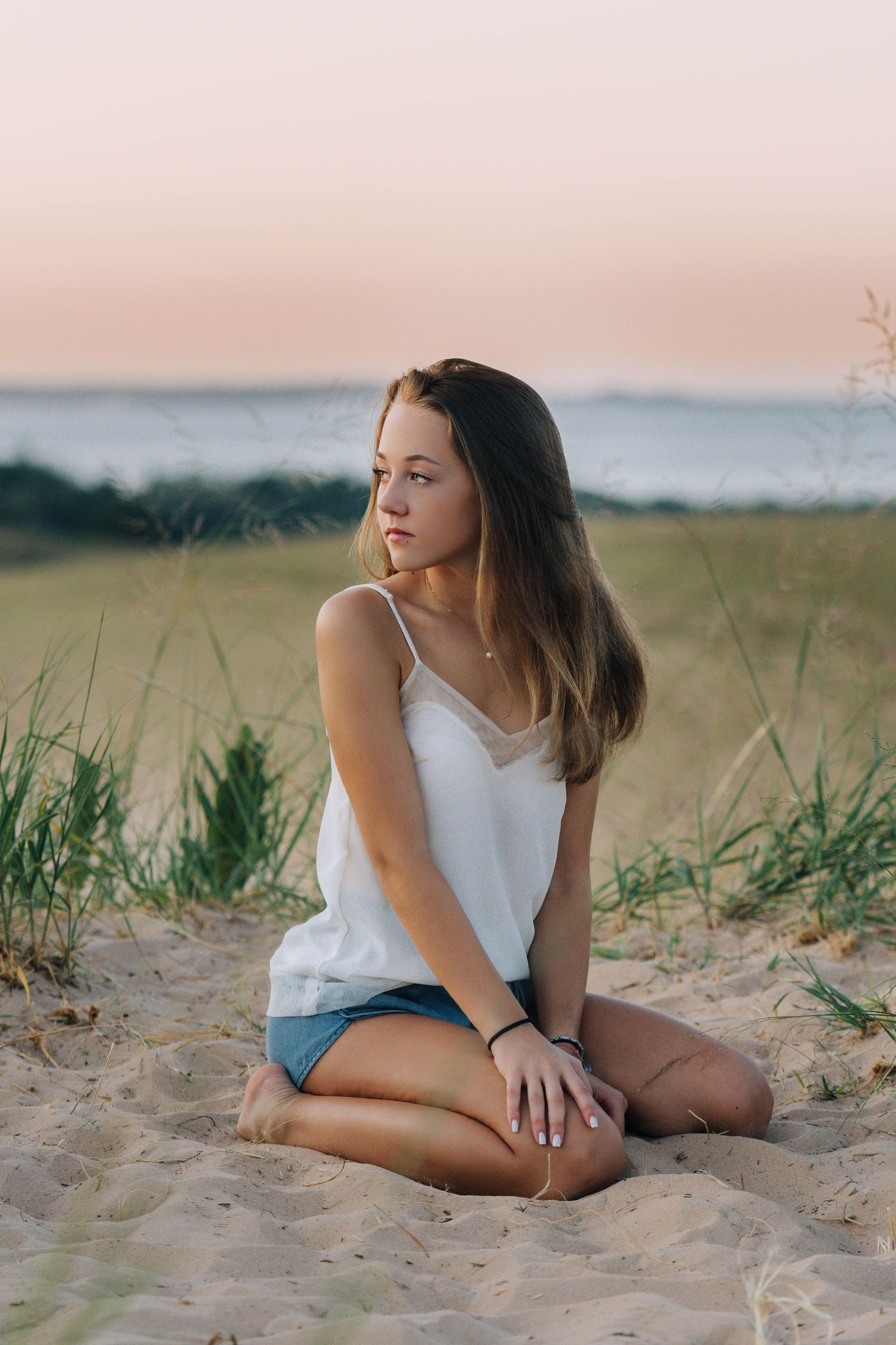 Beachside portrait at sunset with sand dunes and ocean in soft pink light.