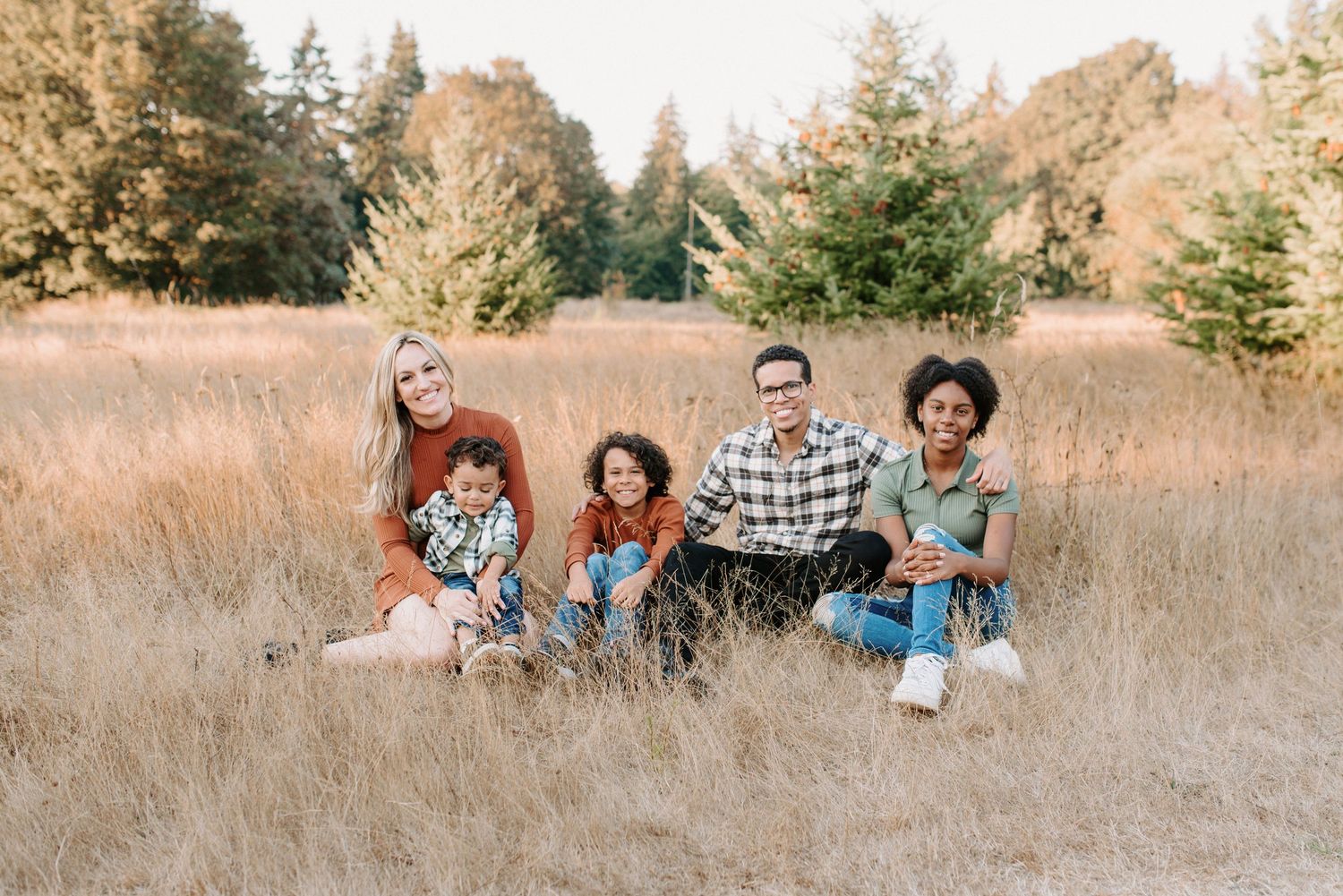 Family relaxing together in tall grass field during golden hour photography session.