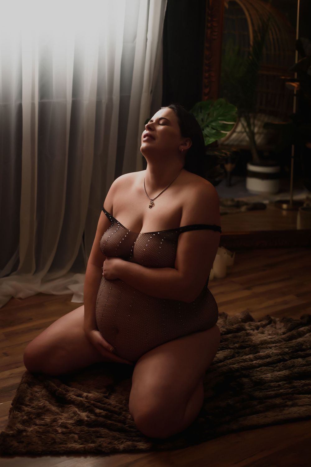 A moody boudoir photo in lingerie with soft window lighting on hardwood floors and a patterned rug.