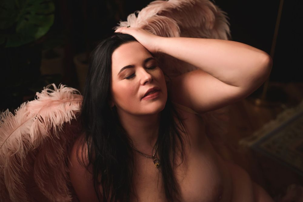 Sensual portrait with pink feathers and moody lighting in dark atmospheric setting.