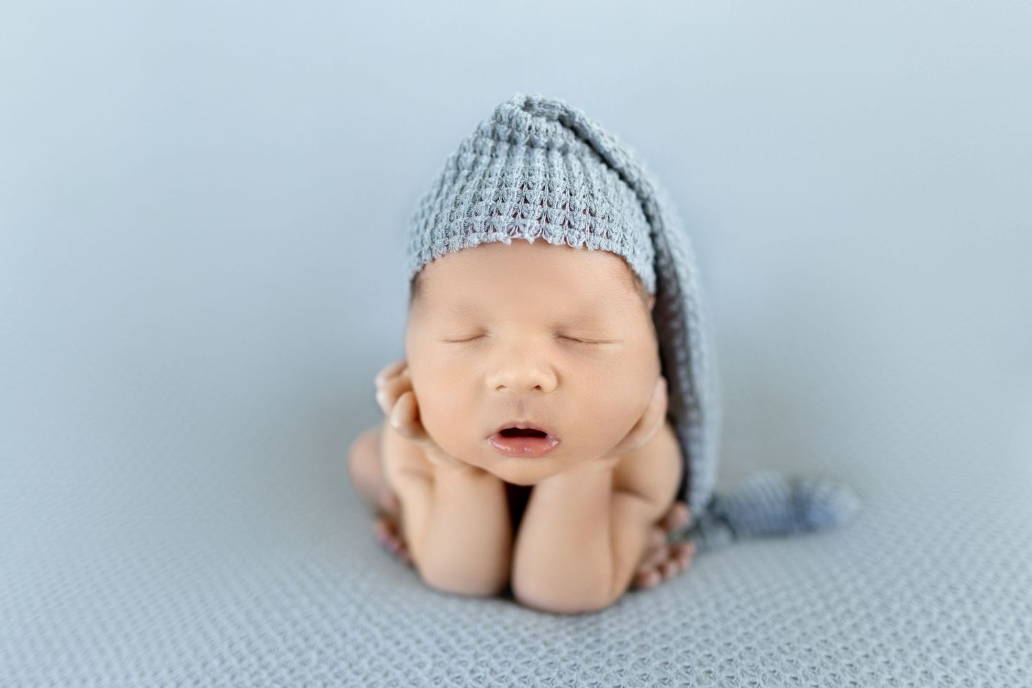 Sleeping newborn baby wearing grey hat with hands gently supporting head.