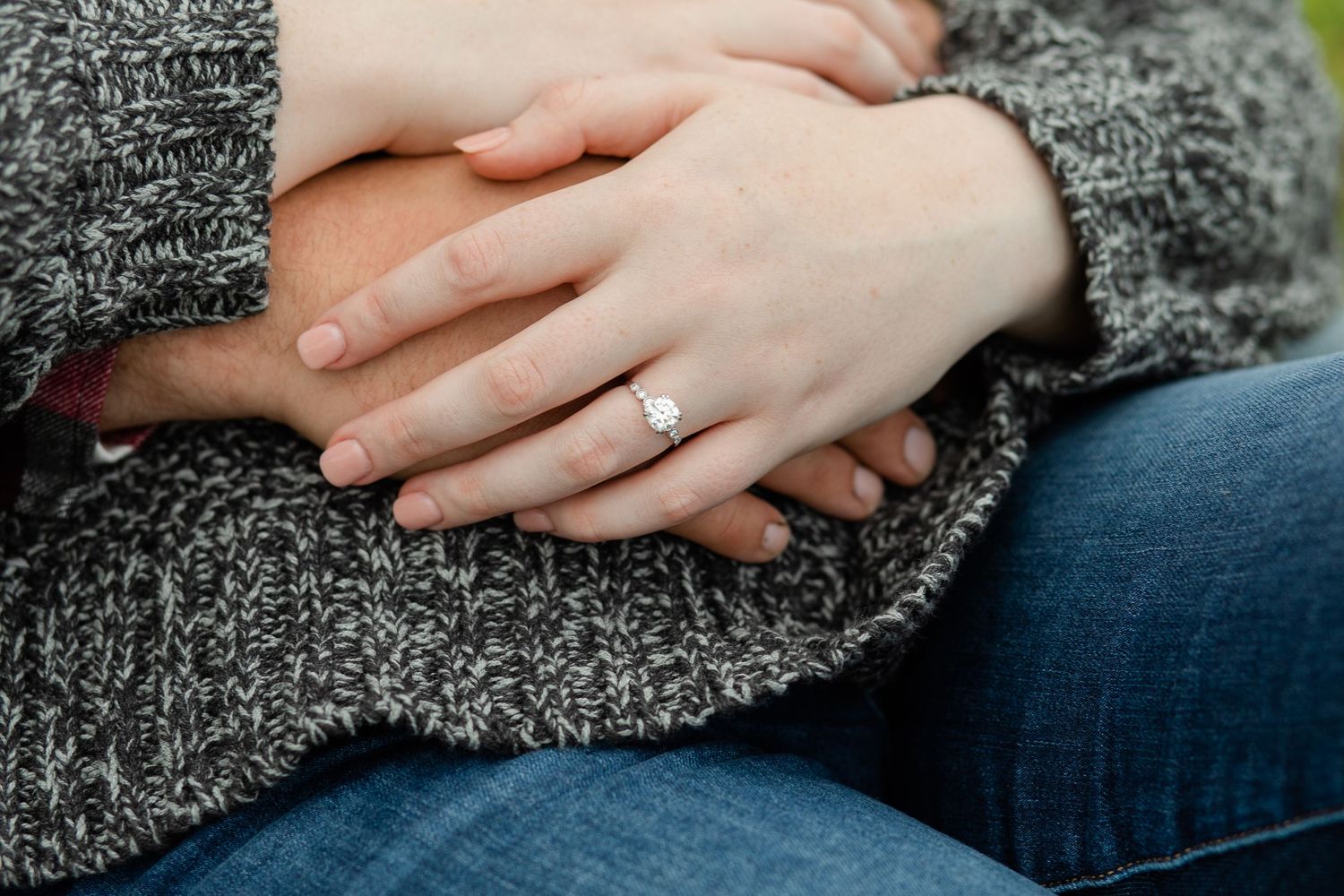 Close-up shot of hands with engagement ring resting on a gray knit sweater.