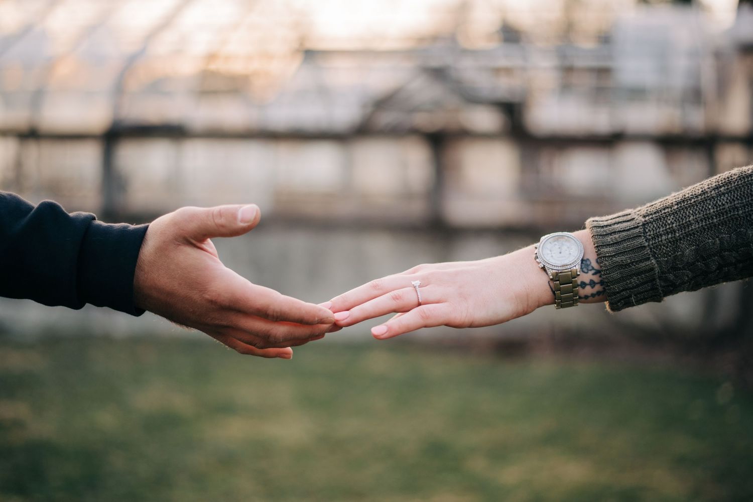 close up photo of man and woman's hands touching at fingertips with engagement ring in focus