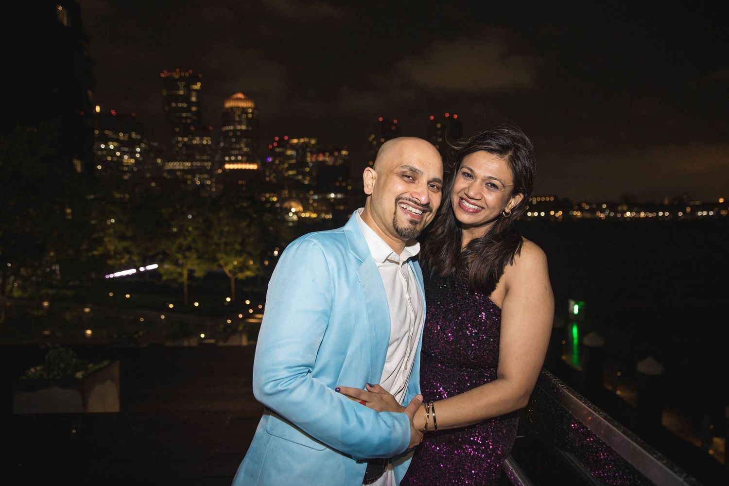 Couple embracing on rooftop terrace with city lights in background at night.