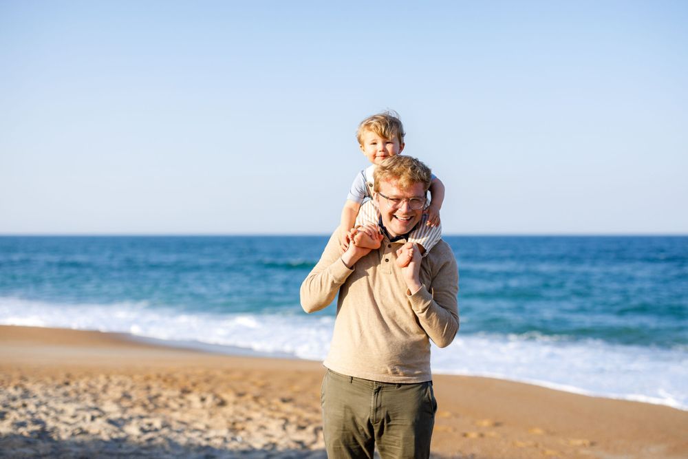 Father with toddler son on his shoulders on a beach