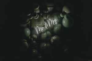 Neon Mr & Mrs sign glows among balloons at wedding reception.