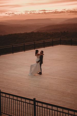 Couple shares an intimate dance moment on a deck overlooking mountains at sunset.