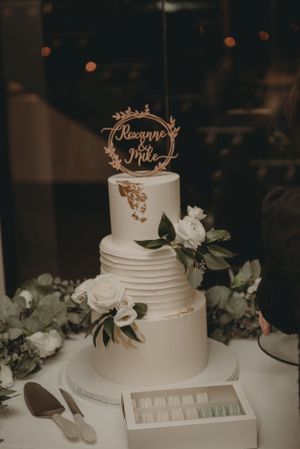 Elegant three-tier white wedding cake with floral decorations and custom topper.